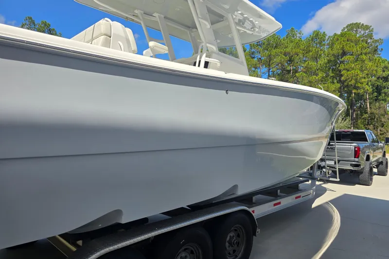 Slide: The Image of 2022 Invincible 33 Catamaran on trailer, parked outdoors with trees in background. - 6