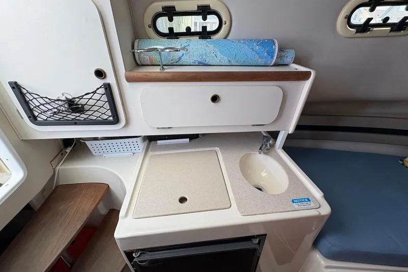 Slide: The Image of 2001 Pursuit 2870 Walkaround cabin interior with sink, storage, and nautical chart. - 28