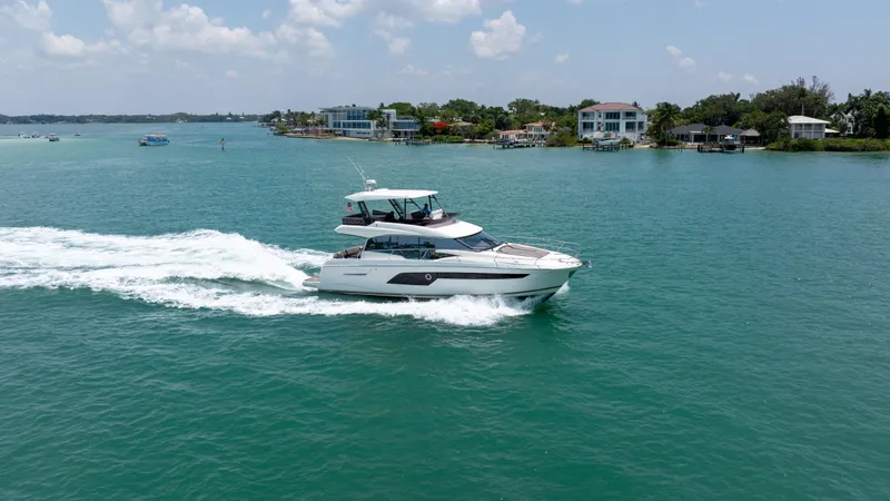 Slide: The Image of 2019 Prestige 520 Flybridge yacht cruising on a sunny day near coastal homes. - 2