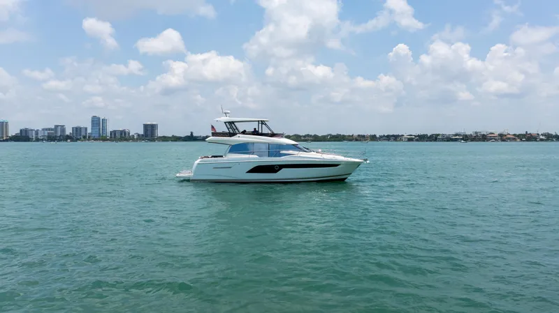 Slide: The Image of 2019 Prestige 520 Flybridge yacht cruising on a calm sea with city skyline in the background. - 4
