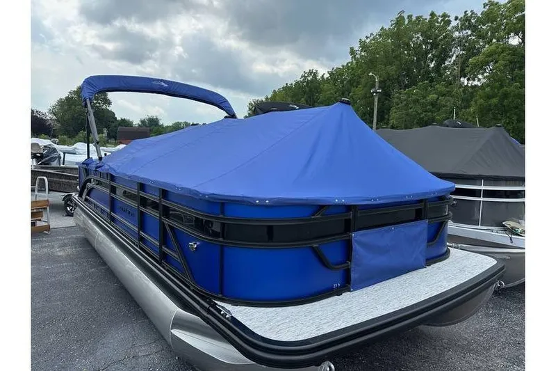 Slide: The Image of 2026 Bennington 23 SF Family pontoon boat with blue cover, parked outdoors. - 45