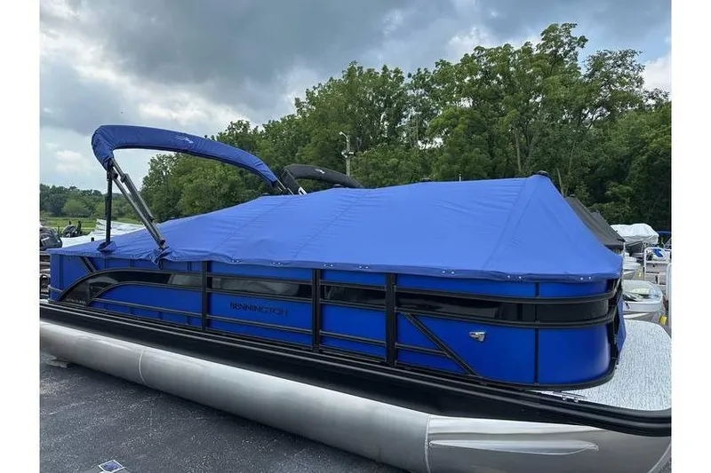 Slide: The Image of 2026 Bennington 23 SF Family pontoon boat with blue cover, parked outdoors. - 46