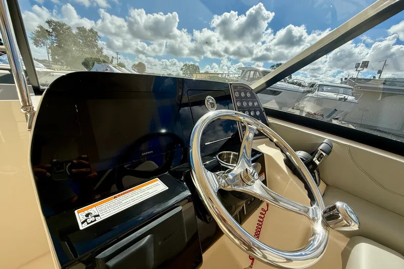 Slide: The Image of 2026 Scout 255 Dorado boat helm with steering wheel and control panel under sunny skies. - 19
