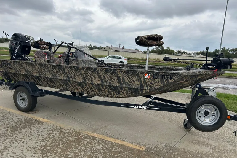 Slide: The Image of 2016 Lowe Roughneck 1756SC camo boat on trailer, parked outdoors under cloudy sky. - 2