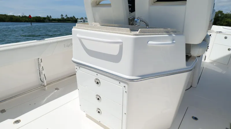 Slide: The Image of 2017 Edgewater 262CC boat interior with storage compartments and sink, docked on calm water. - 26