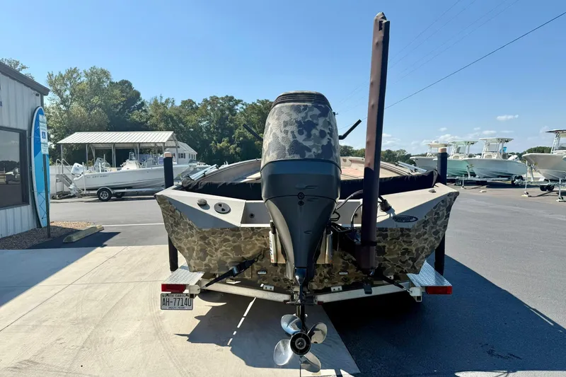 Slide: The Image of 2019 Excel 230 Bay Pro boat with camouflage design, parked on a trailer at a marina. - 2