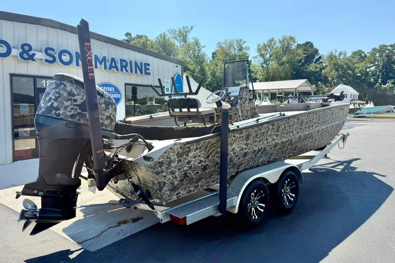 Slide: The Image of 2019 Excel 230 Bay Pro boat with camouflage design on a trailer outside a marine shop. - 45