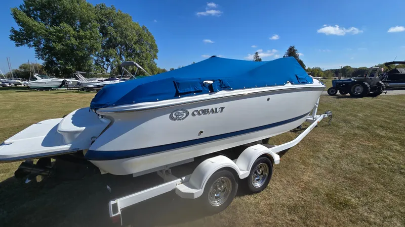 Slide: The Image of 2013 Cobalt 210 boat on trailer with blue cover, parked on grass under clear sky. - 2