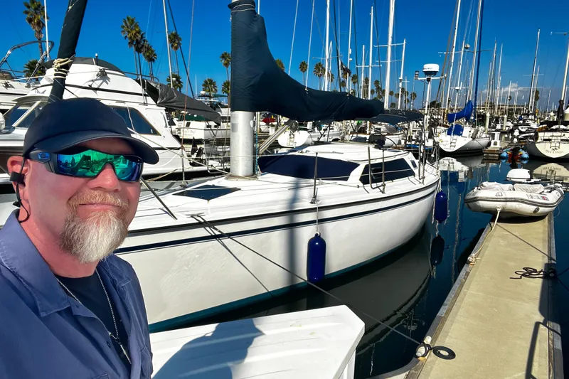 Slide: The Image of Man smiling beside 1989 Hunter Vision 32 sailboat in marina. - 10