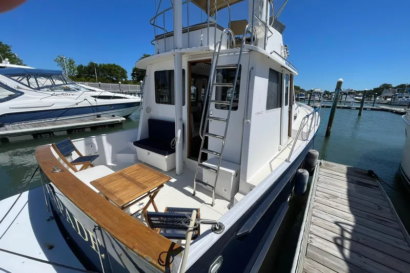 Slide: The Image of 1999 Legacy Yachts 40 Sedan docked, featuring outdoor seating and ladder access. - 103