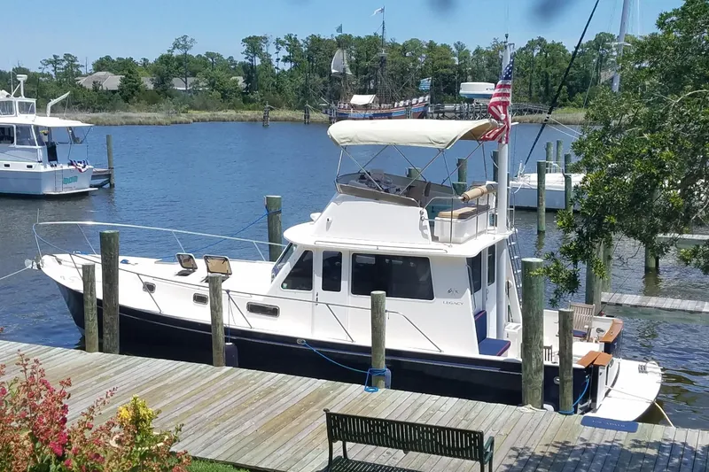 Slide: The Image of 1999 Legacy Yachts 40 Sedan docked by a scenic waterfront with trees and other boats. - 34