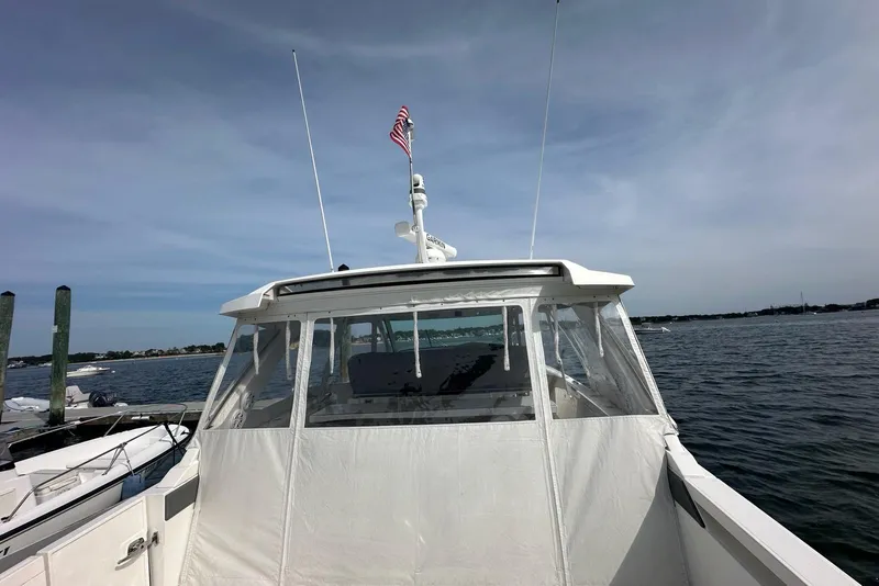 Slide: The Image of 2021 Tiara Sport 43 LS boat docked with American flag, clear sky, and calm waters. - 40