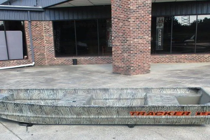The Image of 2026 Tracker Grizzly 15 Jon boat with camouflage design outside a brick building. - 1