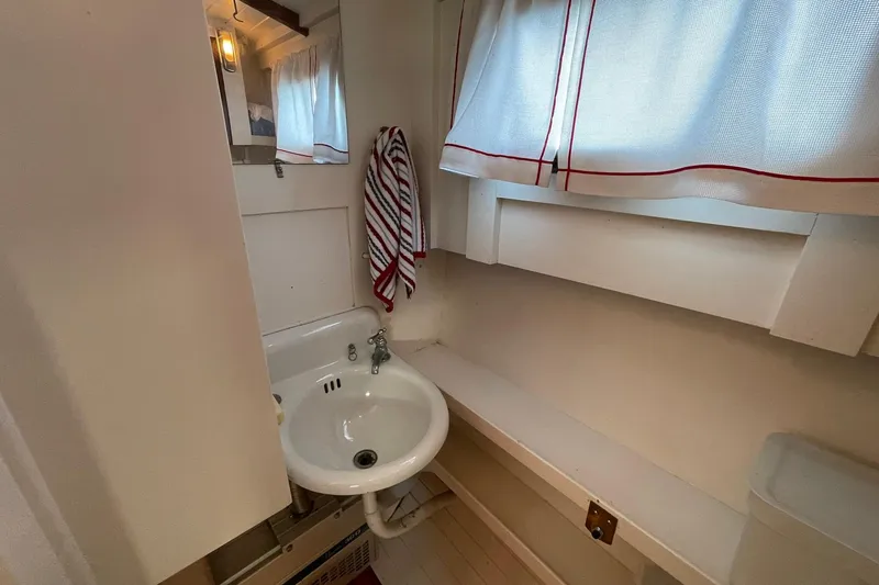 Slide: The Image of 1939 Richardson 26 Little Giant boat bathroom with sink, striped towel, and curtained window. - 17