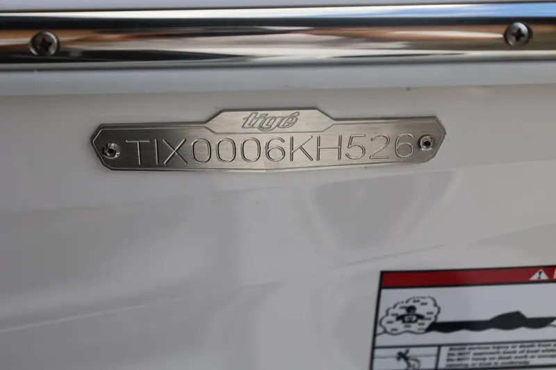 Slide: The Image of Hull identification number on 2026 Tigé 22RZX boat, featuring metal plate and engraved details. - 58
