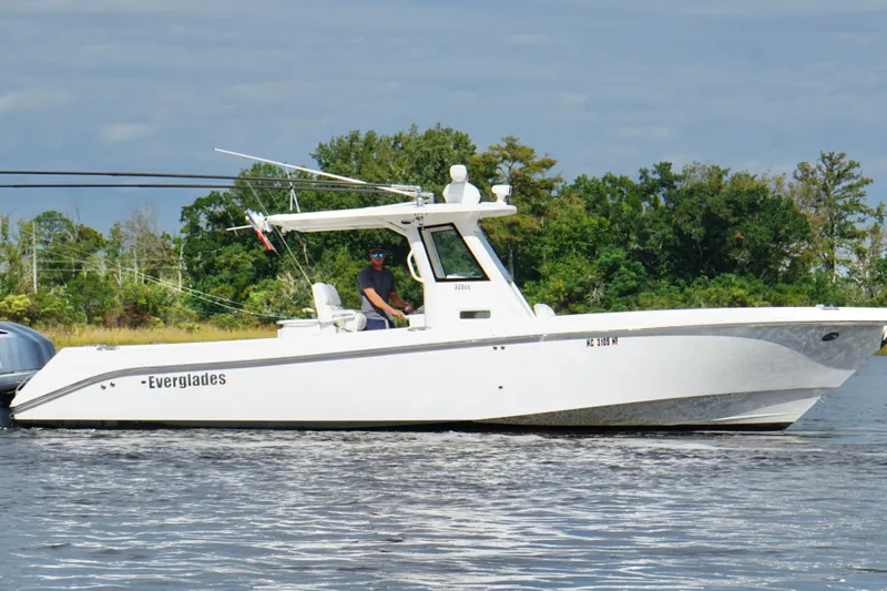 Slide: The Image of 2012 Everglades 325 Center Console boat cruising on a calm lake with lush greenery. - 1