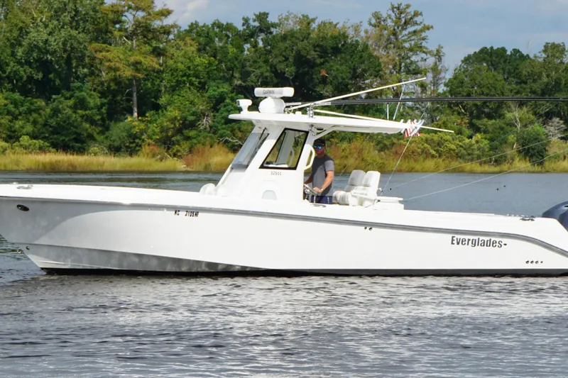 Slide: The Image of 2012 Everglades 325 Center Console boat cruising on a calm lake with lush greenery. - 6