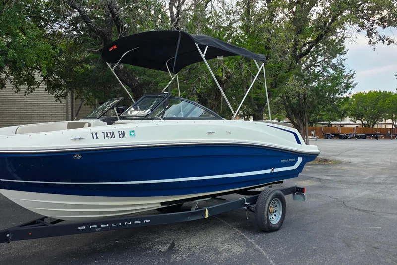 Slide: The Image of 2019 Bayliner VR4 Bowrider I/O boat on trailer, parked outdoors with trees in background. - 1