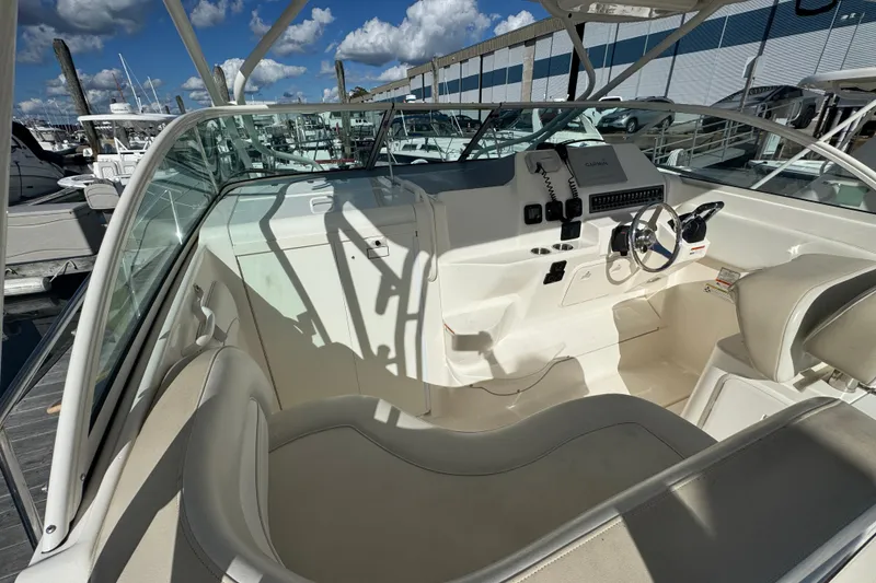 Slide: The Image of 2015 Wellcraft 290 Coastal boat cockpit with steering wheel and seating, docked under blue sky. - 10