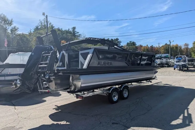 Slide: The Image of 2026 Alera M23Q pontoon boat on trailer in sunny outdoor setting. - 2