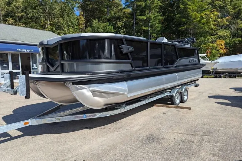 Slide: The Image of 2026 Alera M23Q pontoon boat on trailer, parked outdoors near trees. - 5