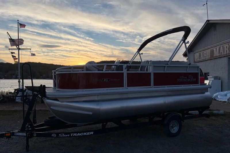 Slide: The Image of 2026 Sun Tracker Bass Buggy 16 XL Select pontoon boat at sunset by a lake. - 83