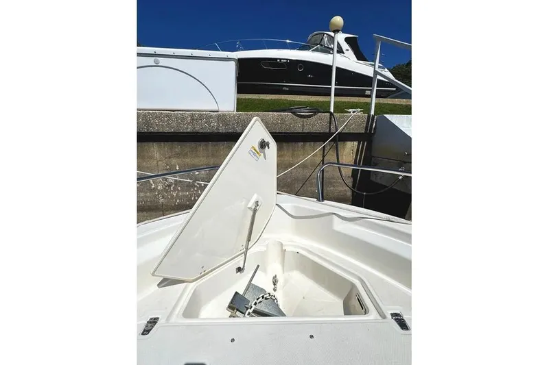 Slide: The Image of 2022 Boston Whaler 220 Dauntless boat with open anchor compartment, docked near another vessel. - 21