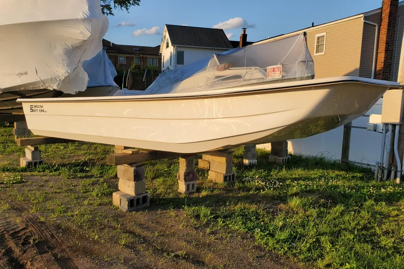Slide: The Image of 2024 Carolina Skiff E24DLX Kit boat on blocks, for sale, in a grassy yard. - 2