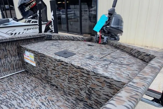 Slide: The Image of 2026 Xpress XTS16 boat with camouflage design and outboard motor, parked outside a building. - 8