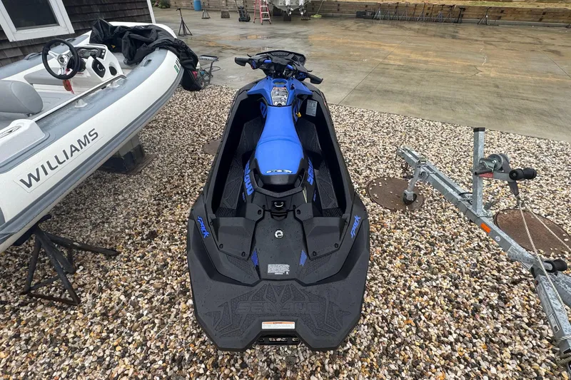 Slide: The Image of 2023 Sea-Doo Spark Trixx jet ski parked on gravel beside a boat and trailer. - 6