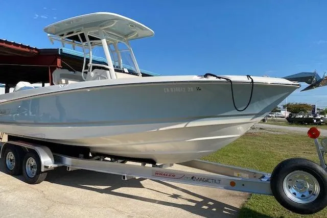 Slide: The Image of 2021 Boston Whaler 230 Outrage boat on trailer, parked outdoors under clear blue sky. - 0