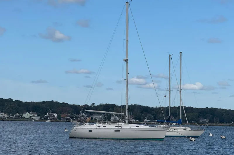 The Image of 1998 Beneteau Oceanis 352 sailboat anchored on calm water under a clear blue sky. - 0