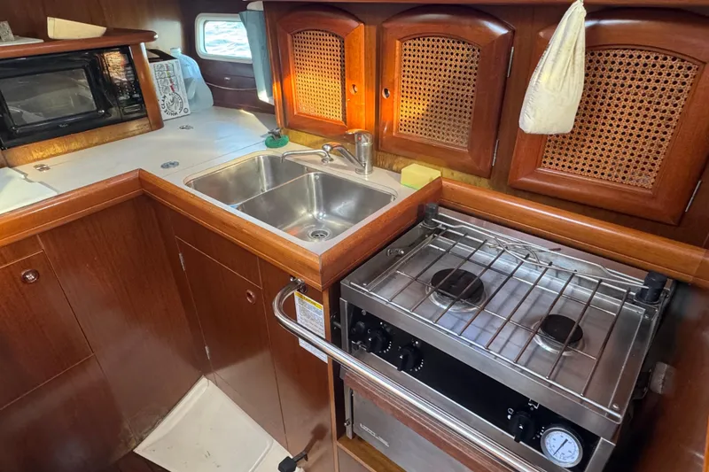 Slide: The Image of 1998 Beneteau Oceanis 352 yacht kitchen with stove, sink, and wooden cabinets. - 27