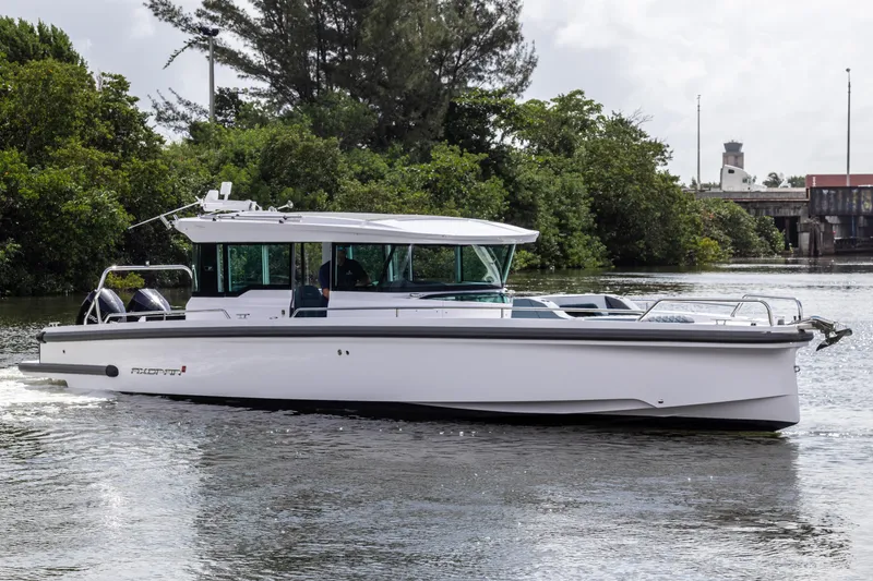 The Image of 2024 Axopar 37XC CROSS CABIN cruising on a calm river with lush greenery. - 0