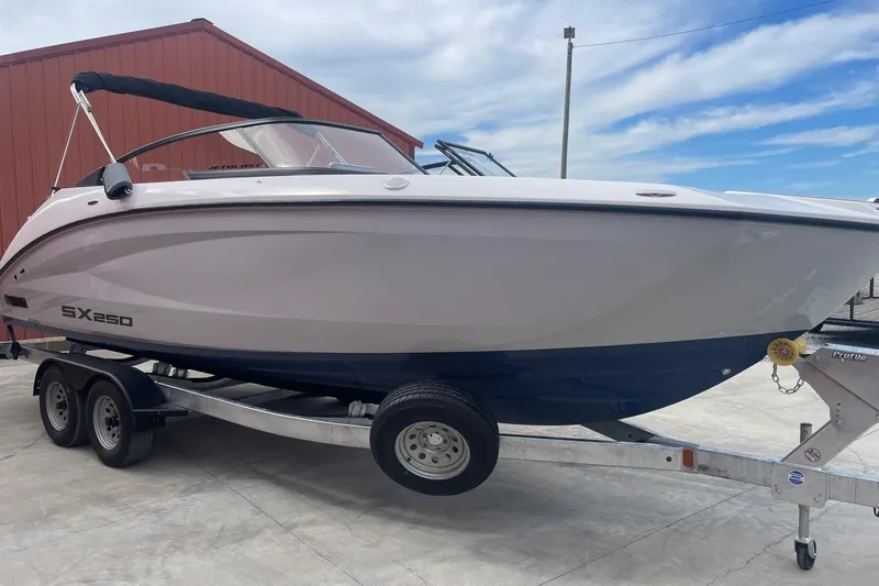 Slide: The Image of 2024 Yamaha Boats SX250 on trailer, parked outdoors near a red building. - 7