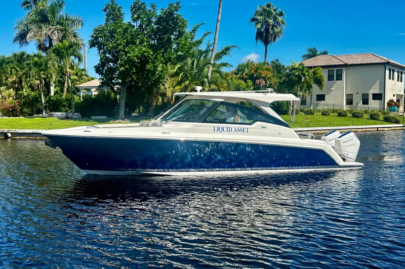 The Image of 2024 Tiara Yachts 34 LX on water, surrounded by lush greenery and waterfront homes. - 2