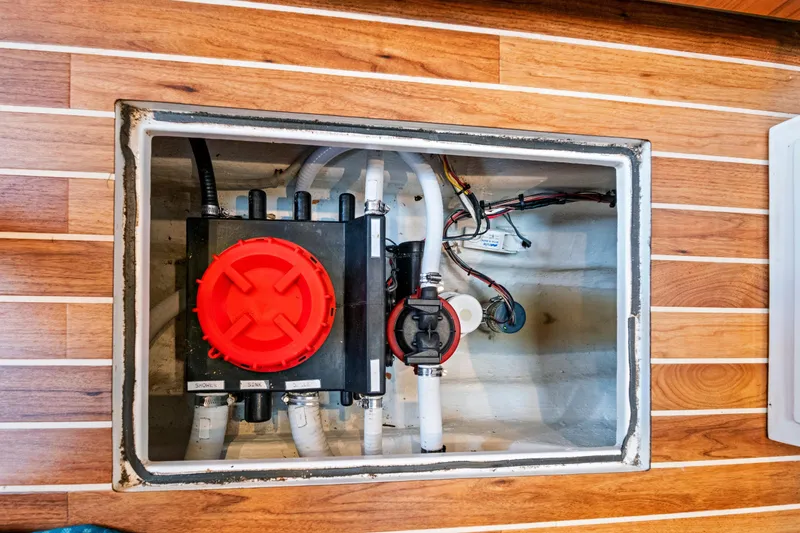 Slide: The Image of Boat bilge compartment with plumbing and wiring, featuring a red valve, on wooden flooring. - 55