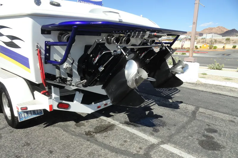 Slide: The Image of 1998 Baja 29 Outlaw boat on trailer, dual propellers, parked in sunny lot. - 28