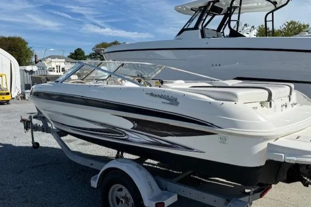 Slide: The Image of 2009 Glastron GT 185 boat on trailer, parked outdoors, with another boat in the background. - 2