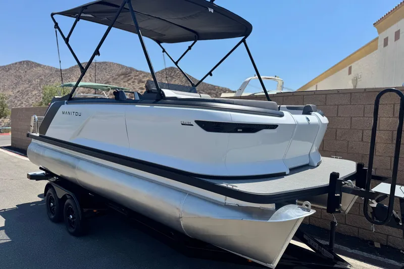 Slide: The Image of 2025 Manitou Cruise 20 pontoon boat on trailer, parked outdoors under clear sky. - 1
