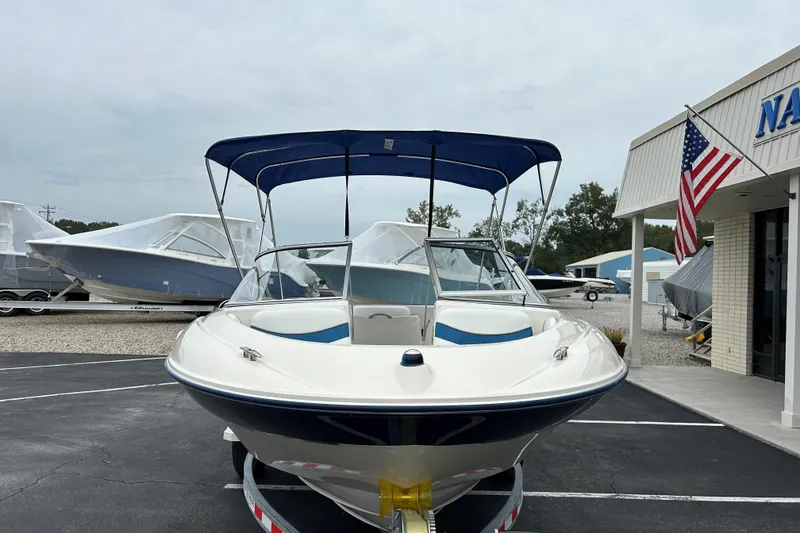Slide: The Image of 2002 Bayliner 195 Capri boat with blue canopy, parked near a nautical store. - 2