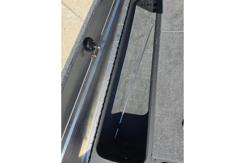 Slide: The Image of 2024 Tracker Pro Team 190 TX boat storage compartment with rod holder, gray carpet interior. - 16