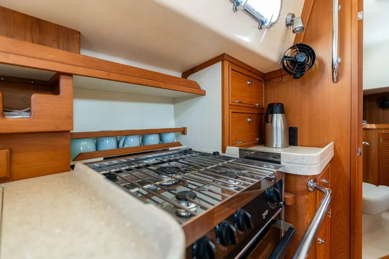 Slide: The Image of 2008 Island Packet 465 yacht kitchen with stove, wooden cabinetry, and countertop. - 12