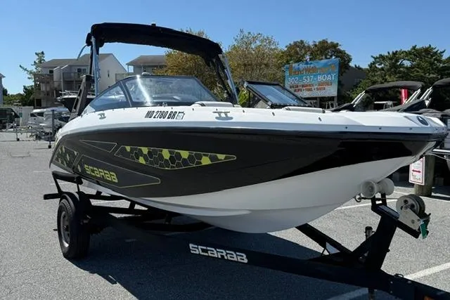 Slide: The Image of 2020 Scarab 195 ID boat on trailer, parked outdoors in a marina setting. - 2