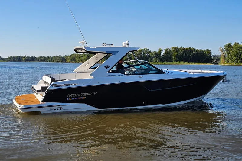 Slide: The Image of 2022 Monterey 378SS Super Sport boat on calm water, clear sky, lush green shoreline. - 2
