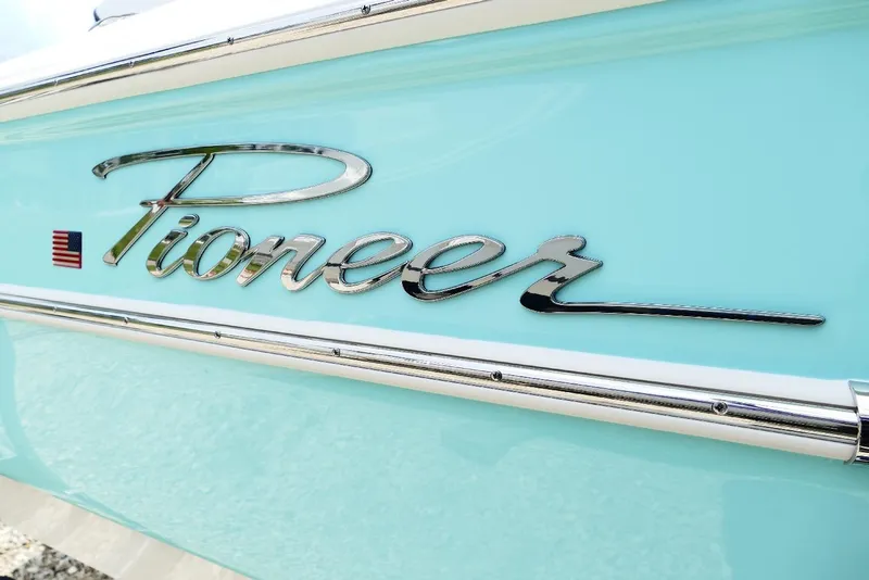 Slide: The Image of 2026 Pioneer 220 Bay Sport boat logo on light blue hull with American flag. - 51