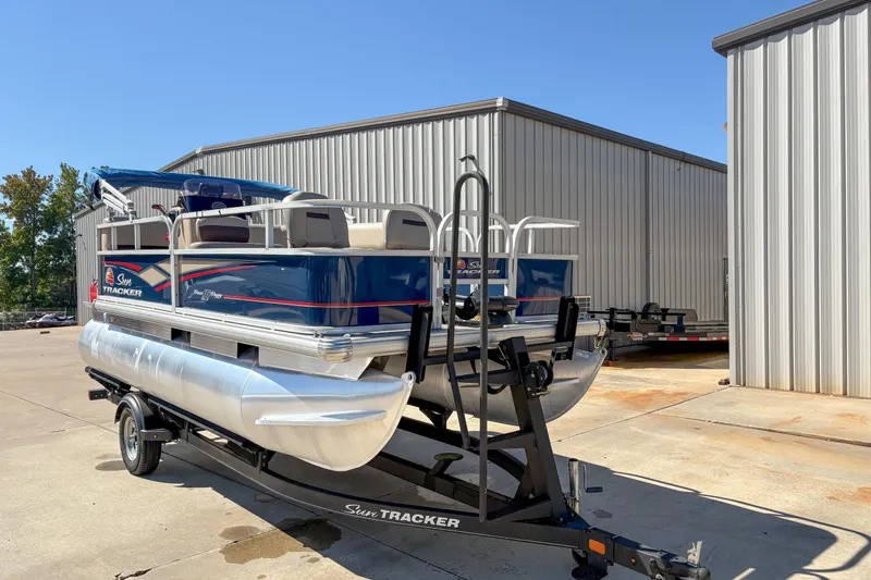 Slide: The Image of 2019 Sun Tracker Bass Buggy 16 DLX pontoon boat on trailer, parked outside metal building. - 2