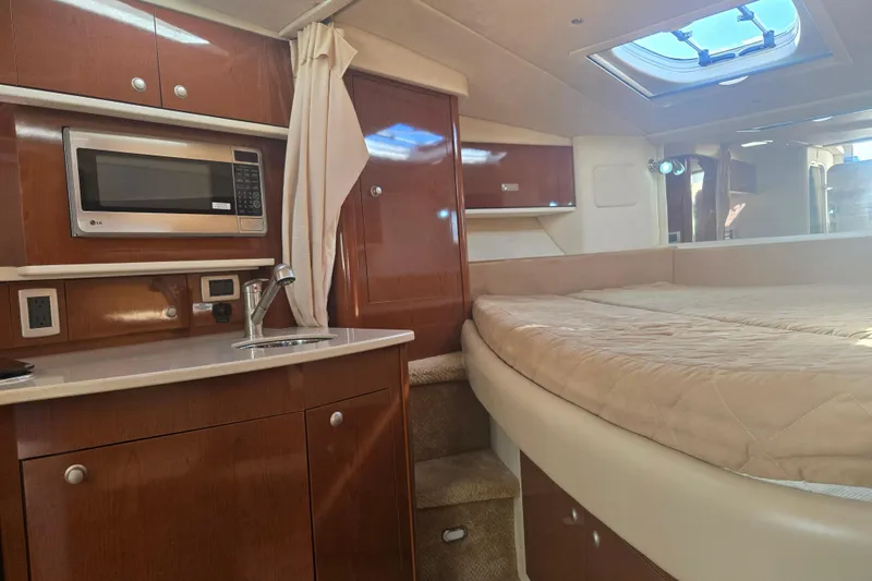Slide: The Image of 2010 Sea Ray 330 Sundancer cabin interior with kitchenette and bed, featuring wood cabinetry. - 45