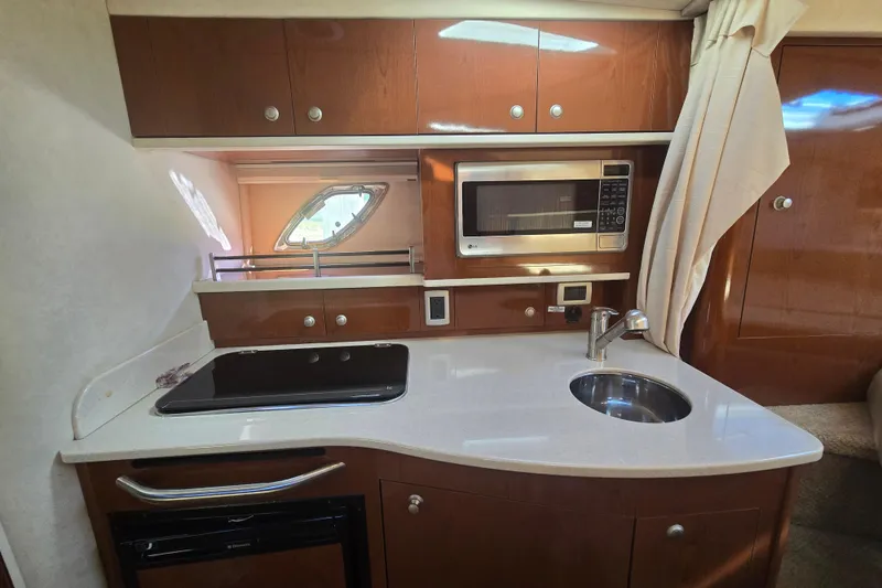Slide: The Image of 2010 Sea Ray 330 Sundancer kitchen with microwave, sink, and stove in wooden cabinetry. - 50