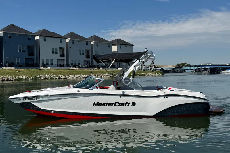 The Image of 2021 MasterCraft X22 boat on calm water near modern buildings. - 0